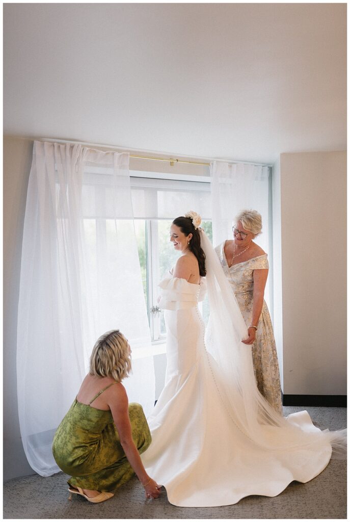 bride's mom and sister helping her put on the dress